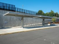 the empty road has a wooden structure beside it with metal barriers around it and a black iron fence surrounding