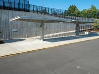 the empty road has a wooden structure beside it with metal barriers around it and a black iron fence surrounding