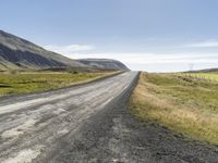 an empty road between two mountains in the far distance, with a fence and a green grass hill