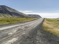 an empty road between two mountains in the far distance, with a fence and a green grass hill