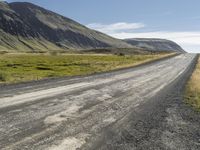 an empty road between two mountains in the far distance, with a fence and a green grass hill