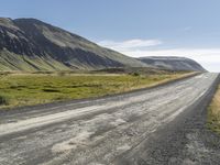 an empty road between two mountains in the far distance, with a fence and a green grass hill