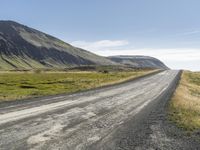 an empty road between two mountains in the far distance, with a fence and a green grass hill