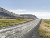 an empty road between two mountains in the far distance, with a fence and a green grass hill