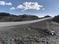 the empty road leading up to a mountain is surrounded by rocks and mountains under a blue sky