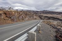 there is an empty road going past some mountains and a snow - capped mountain range