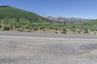 an empty road next to a mountain with mountains in the background as seen from an outside corner