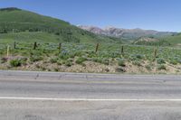 an empty road next to a mountain with mountains in the background as seen from an outside corner