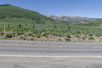 an empty road next to a mountain with mountains in the background as seen from an outside corner