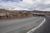 the road is empty of vehicles on a sunny day with mountains in the background at a point where there are snow capped peaks