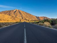 the road to el teide is empty on the desert land, with mountains in the background