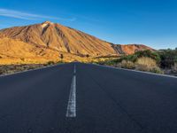 the road to el teide is empty on the desert land, with mountains in the background