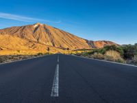 the road to el teide is empty on the desert land, with mountains in the background