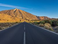 the road to el teide is empty on the desert land, with mountains in the background