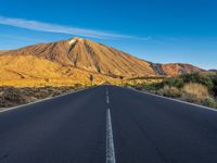 the road to el teide is empty on the desert land, with mountains in the background