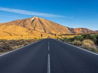 the road to el teide is empty on the desert land, with mountains in the background