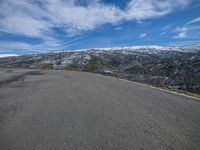 a snow covered mountain side with an empty road and a bright blue sky with clouds