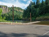 an empty road beside the mountain and a body of water with trees in the background