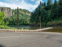 an empty road beside the mountain and a body of water with trees in the background