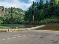 an empty road beside the mountain and a body of water with trees in the background