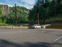 an empty road beside the mountain and a body of water with trees in the background