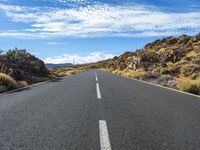 an empty road in a mountainous area with rocky hills and blue sky with white clouds