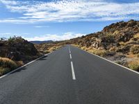 an empty road in a mountainous area with rocky hills and blue sky with white clouds