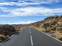 an empty road in a mountainous area with rocky hills and blue sky with white clouds