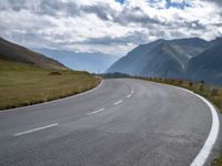 an empty road and mountains with a sign on the side of it's curved road