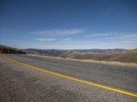 yellow stripe on empty road in mountains area at daytime time with blue sky overhead - high angle view