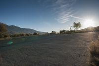 a empty road with the sun coming in over the mountains and trees on one side