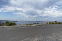 an empty asphalt road with the ocean in the distance in front of it and the trees and bushes along side it