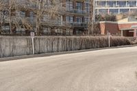 an empty road next to the side of a building with a fence and no parking signs attached to it