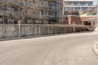 an empty road next to the side of a building with a fence and no parking signs attached to it