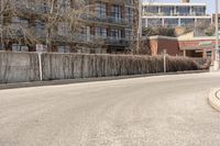 an empty road next to the side of a building with a fence and no parking signs attached to it