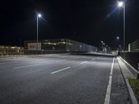 empty road at night with two lights and a fence beside it with benches at the end