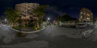 an empty road at night time in a city with cars parked next to it and buildings on both sides