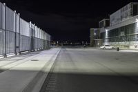 the road is empty at night near a fence and parking lot in front of it