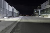 the road is empty at night near a fence and parking lot in front of it