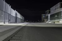 the road is empty at night near a fence and parking lot in front of it