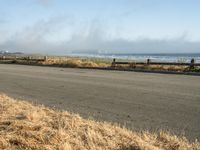 this is an empty road next to the ocean with a man walking on it and a person with surfboard