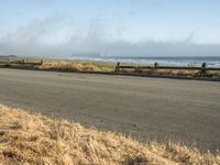 this is an empty road next to the ocean with a man walking on it and a person with surfboard