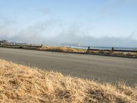 this is an empty road next to the ocean with a man walking on it and a person with surfboard