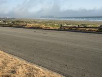 this is an empty road next to the ocean with a man walking on it and a person with surfboard