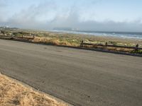 this is an empty road next to the ocean with a man walking on it and a person with surfboard