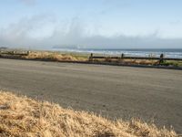 this is an empty road next to the ocean with a man walking on it and a person with surfboard