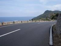 an empty road next to the ocean with the cliffs in the background on top of it