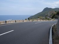 an empty road next to the ocean with the cliffs in the background on top of it