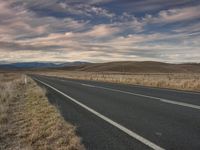 a long empty road leading into the distance in an open field with mountains and fields