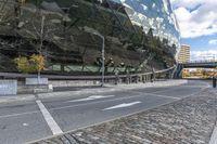 an empty road with a bricked sidewalk in front of an opera building with reflective windows